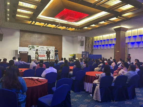 Attendees seated at round tables facing a stage during a TOC family get-together and scientific session.
